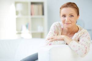 Aromataasinestäjälääkitystä saava nainen istuu sohjalla ja hymyilee.